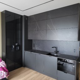 KAROLINA SOŁOBODOWSKA - Nowoczesna, szara kuchnia z czarnymi akcentami: armatura, fronty szafek i blat. Płytki imitujące marmur na ścianie. Widoczna zabudowa piekarnika i szafa.