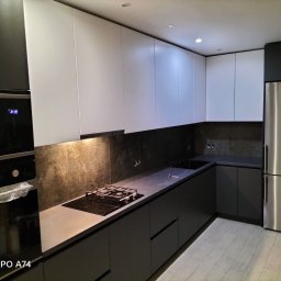 KAROLINA SOŁOBODOWSKA - Nowoczesna kuchnia z szarymi szafkami dolnymi i białymi górnymi, wykończona kamiennym blatem i stalową lodówką. Minimalistyczny design z oświetleniem punktowym.