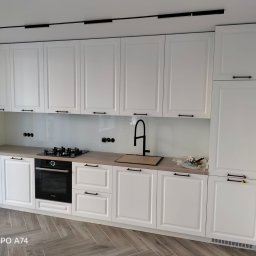 KAROLINA SOŁOBODOWSKA - Biała kuchnia na wymiar z czarnymi akcentami: bateria, uchwyty, płyta grzewcza. Jasny blat i backsplash. Podłoga w jodełkę. Nowoczesny design.