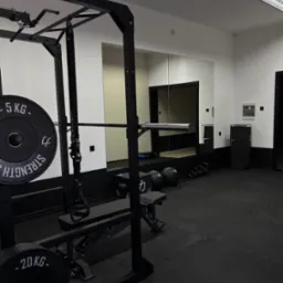 Nowoczesna, czarno-biała siłownia: klatka do ćwiczeń siłowych z obciążeniem, lustro, kettlebells. Minimalistyczny design, profesjonalny sprzęt do treningu.