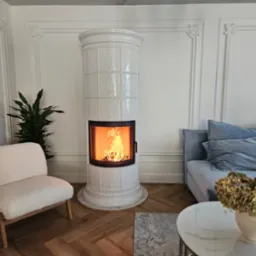 Biały, kaflowy piec kominkowy Schmid Rondo 55 51s w jasnym salonie z drewnianą podłogą w jodełkę i dekoracyjnymi listwami ściennymi. Płomienie wewnątrz.