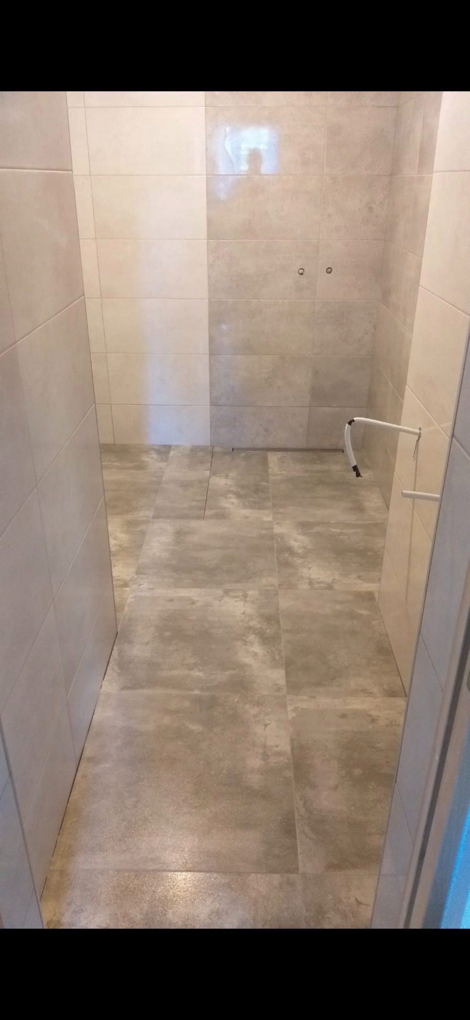 Jasna łazienka po remoncie: beżowe płytki na ścianach i podłodze, widoczne instalacje wodne. Minimalistyczny design, czysta przestrzeń.