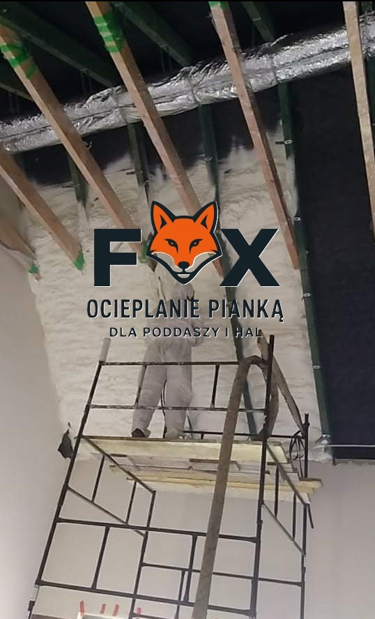 Pracownik w kombinezonie na rusztowaniu, aplikujący piankę PUR na poddaszu z widocznymi elementami konstrukcyjnymi i wentylacją. Ocieplanie pianką.