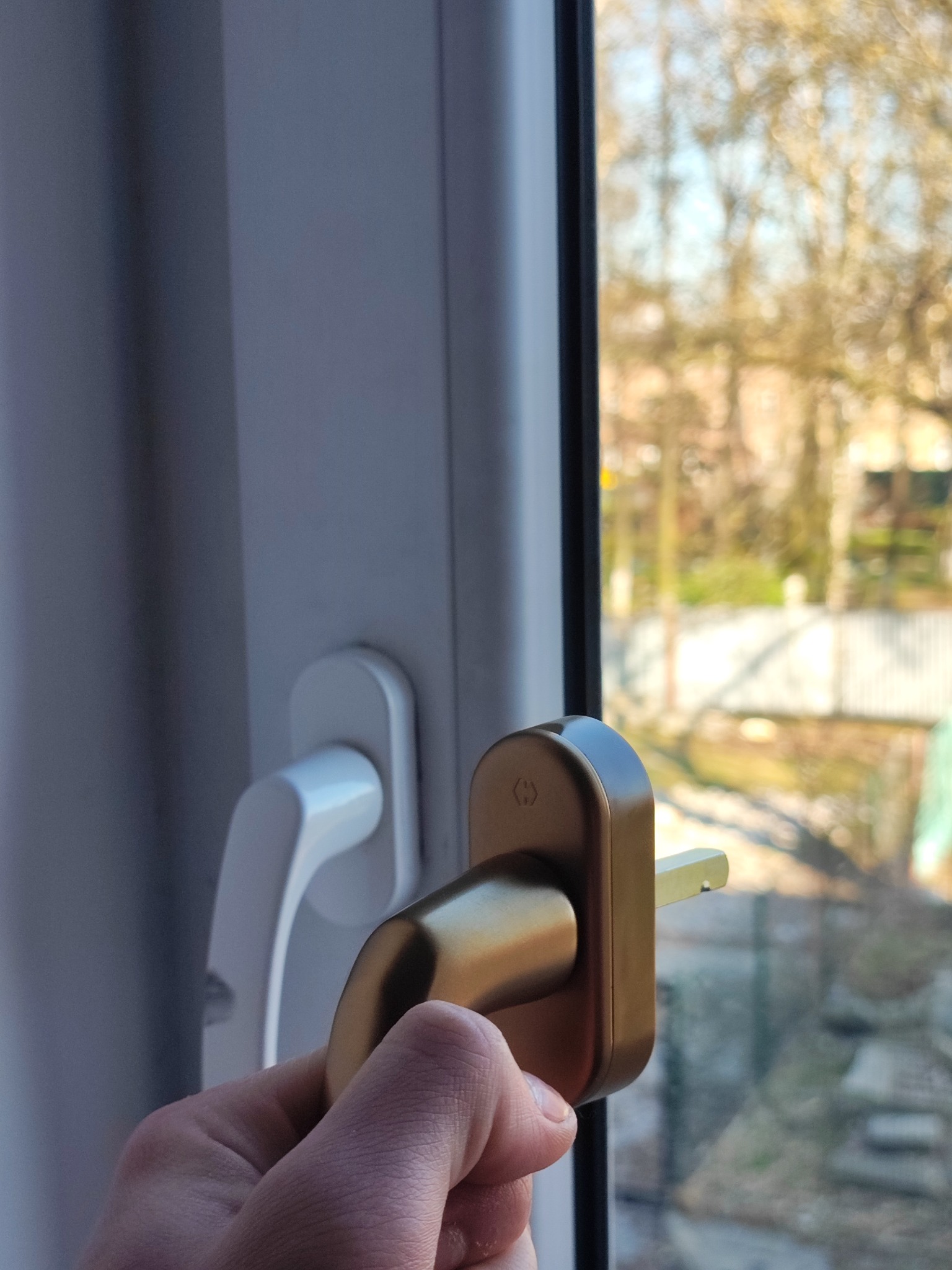 Wymiana klamki okiennej na złotą, widok z bliska na dłoń trzymającą nową klamkę. W tle widok na zewnątrz przez okno.