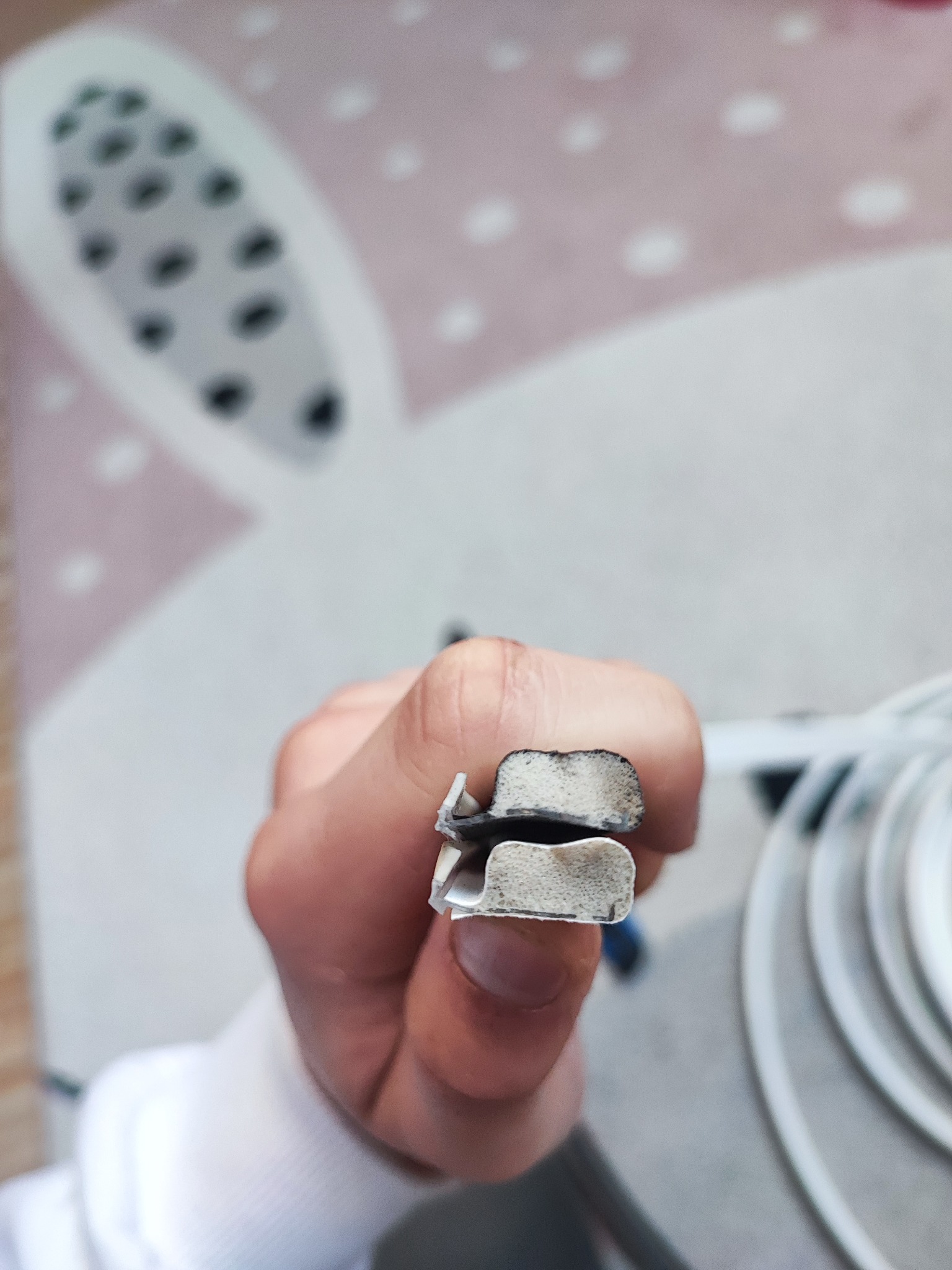 Detail dłoni trzymającej uszczelkę okienną z widocznymi śladami zużycia, na tle dywanu z motywem królika. Bliski kadr, ukazujący strukturę materiału.