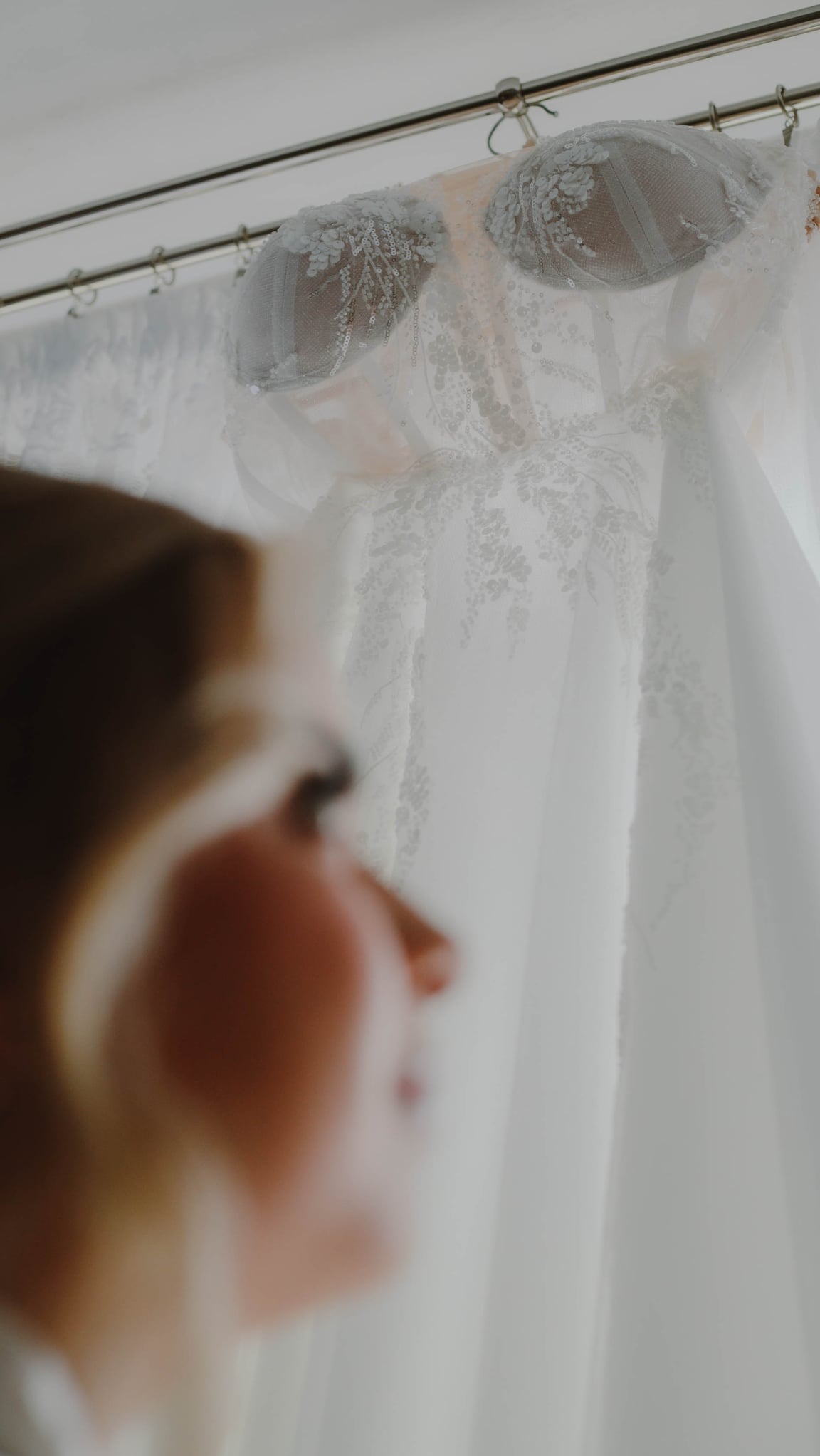 Suknia ślubna z koronkowym gorsetem, wisząca na wieszaku, uchwycona z perspektywy panny młodej w Iwierzycach. Delikatne światło podkreśla detale.