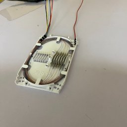 LinkSat Serwis Anten i Światłowodów - Rozdzielnica światłowodowa z widocznymi włóknami w różnych kolorach, ułożonymi wewnątrz białej obudowy. Obok leżą szczypce do cięcia kabli.