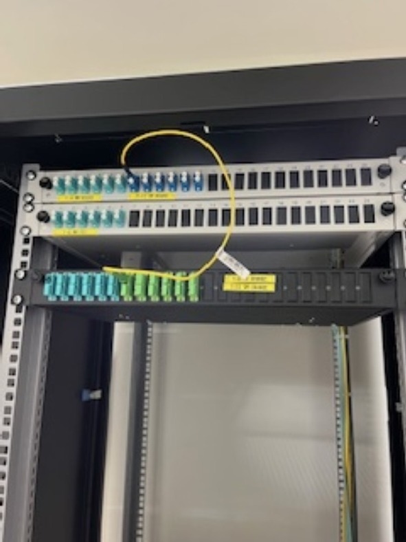 Panel krosowniczy światłowodowy w szafie rack z podłączonymi kablami światłowodowymi. Widoczne porty z wpiętymi złączami. Oznakowane porty.