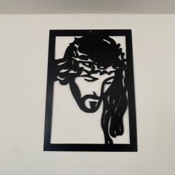 Ogrodzenia Mikołaj Jóźwik - Czarna, metalowa dekoracja ścienna przedstawiająca wizerunek Jezusa w koronie cierniowej, umieszczona na białej ścianie. Minimalistyczny design, wyraźne kontury.
