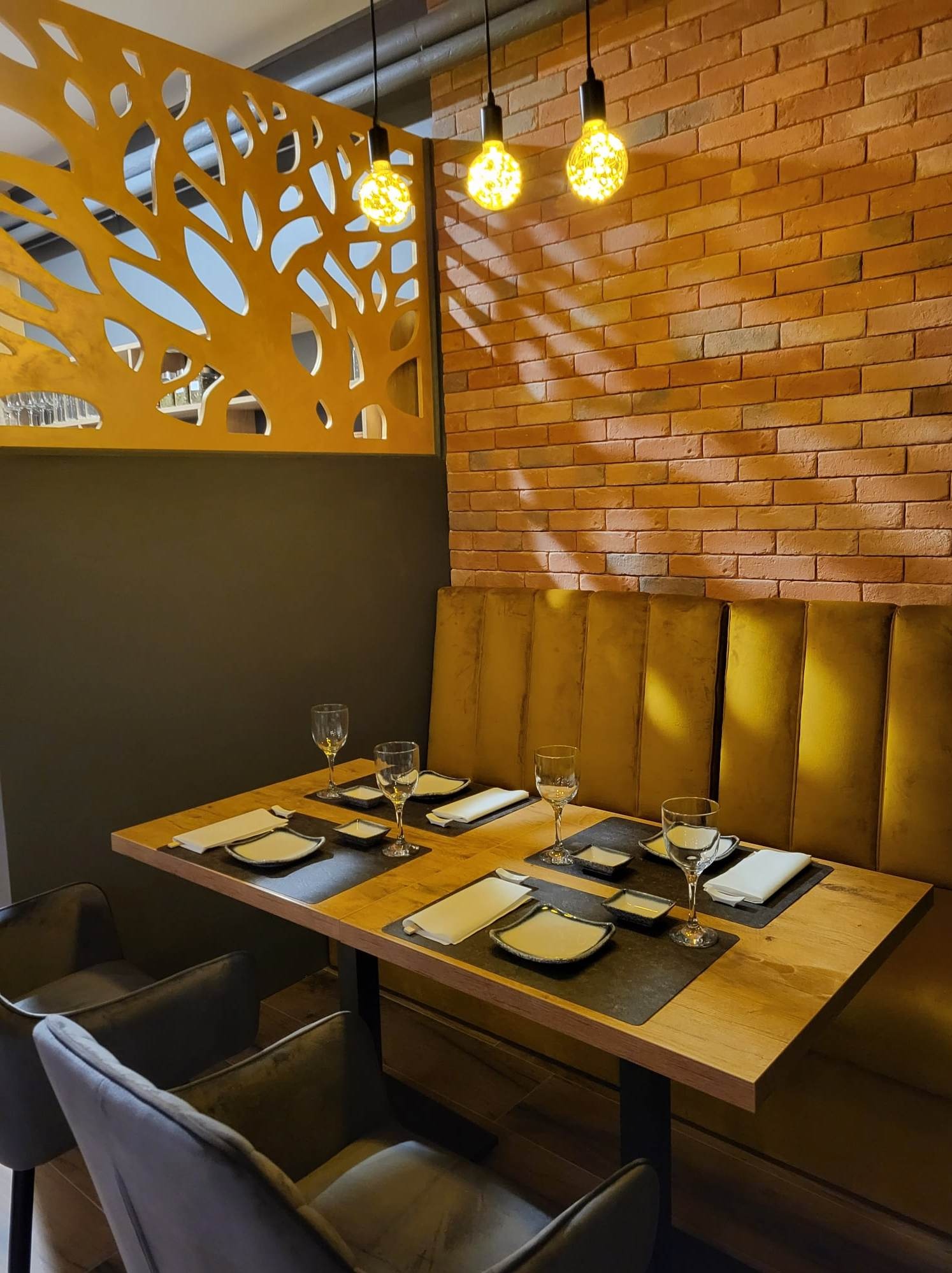 Ustawiony stół w restauracji z ceglaną ścianą i dekoracyjną ścianką działową z motywem drzewa. Oświetlenie stanowią żarówki w stylu retro.