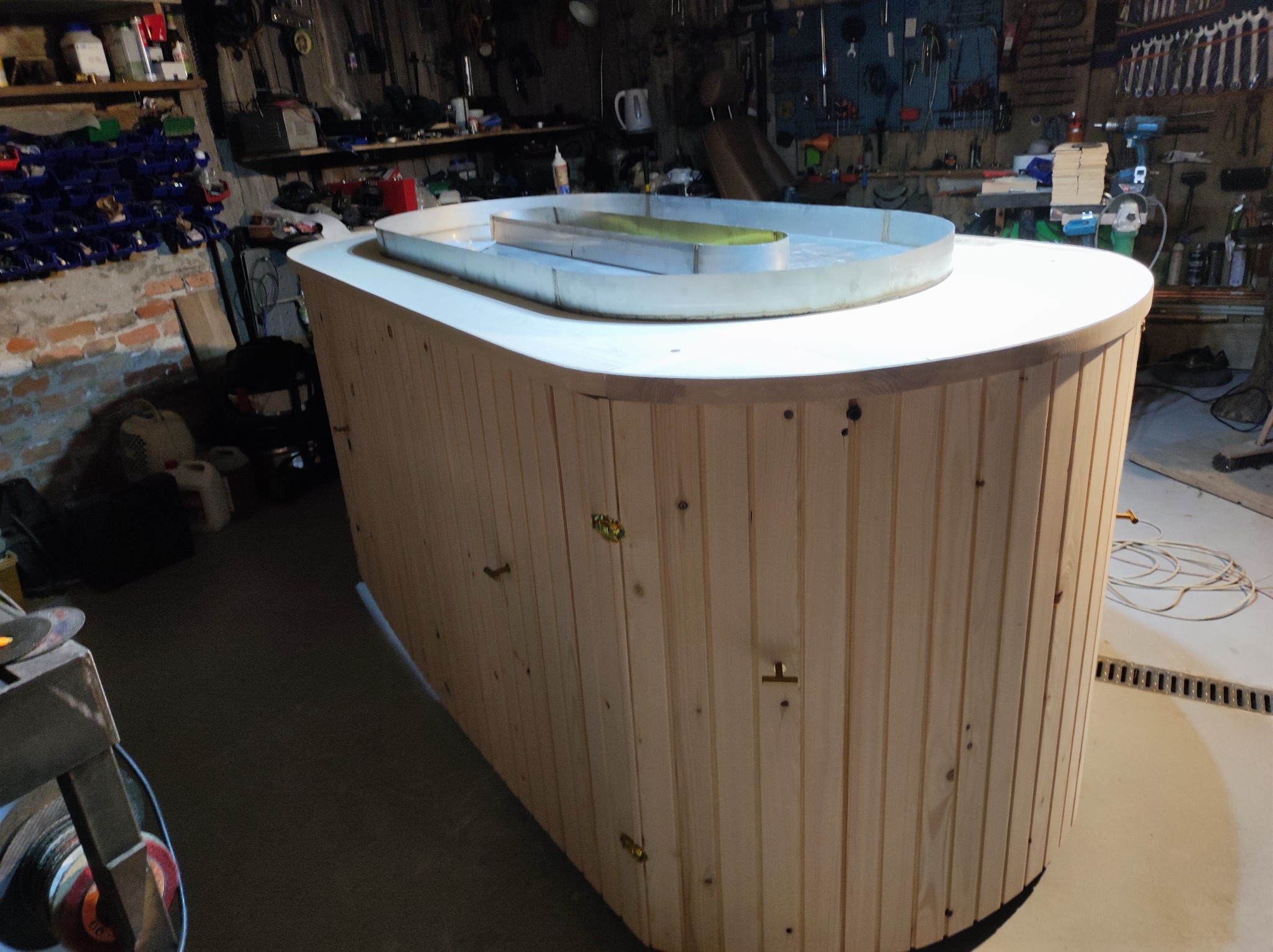 Drewniana obudowa w warsztacie z metalową formą na wierzchu. Widoczne narzędzia i akcesoria warsztatowe w tle, co sugeruje etap tworzenia.