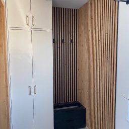 HolzForm Tomasz Jaśko - Biała szafa z połyskiem i czarna szafka na buty, uzupełnione dekoracyjną ścianą z drewnianych lameli w przedpokoju. Nowoczesny design.