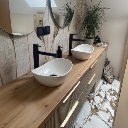 HolzForm Tomasz Jaśko - Nowoczesna łazienka z drewnianym blatem, dwiema białymi umywalkami i czarnymi bateriami. Uwagę przykuwają marmurowe płytki podłogowe i designerskie lustro.