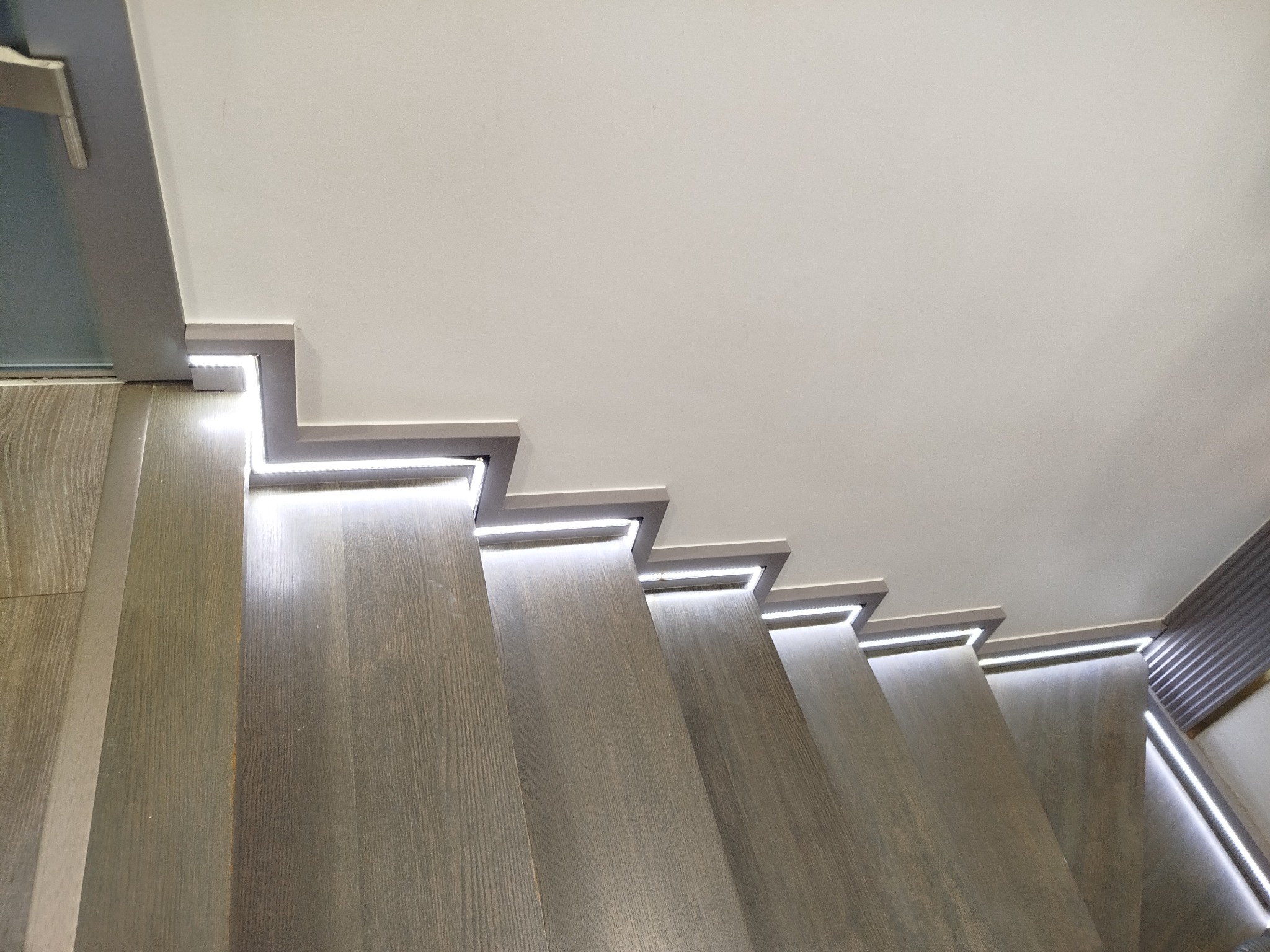 Schody z drewnianymi stopniami i oświetleniem LED wzdłuż krawędzi, widok z góry, nowoczesny design, jasne światło, szare wykończenie.