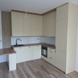 Krystian Suchoparski - Jasna kuchnia z drewnianym blatem i czarną armaturą. Uwagę przykuwają minimalistyczne fronty szafek i drewniane panele dekoracyjne na ścianie.