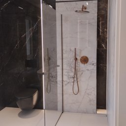 Metr za metrem - Nowoczesna łazienka z kabiną typu walk-in, wykończona marmurem w odcieniach bieli i czerni. Miedziana armatura i subtelne oświetlenie LED podkreślają elegancję wnętrza.