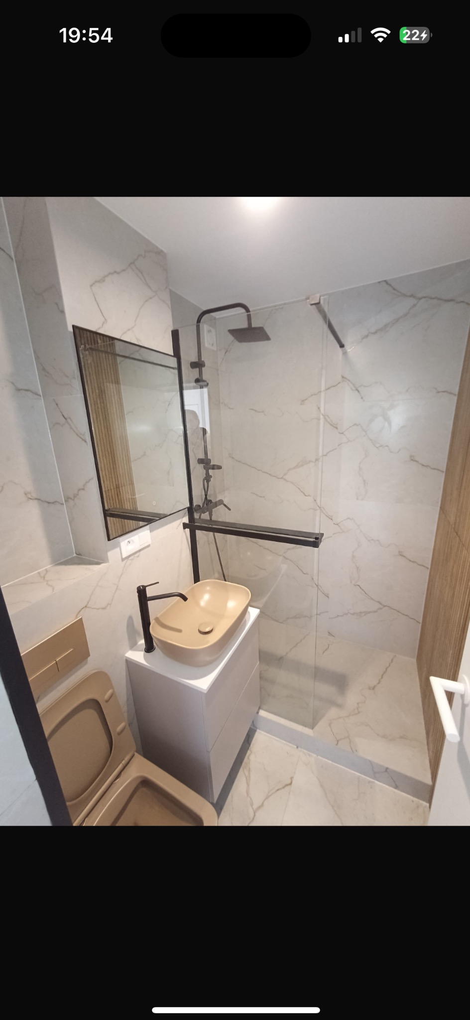 Nowoczesna łazienka z beżową umywalką nablatową i kabiną prysznicową typu walk-in. Płytki imitujące marmur na ścianach i podłodze. Armatura w kolorze czarnym.