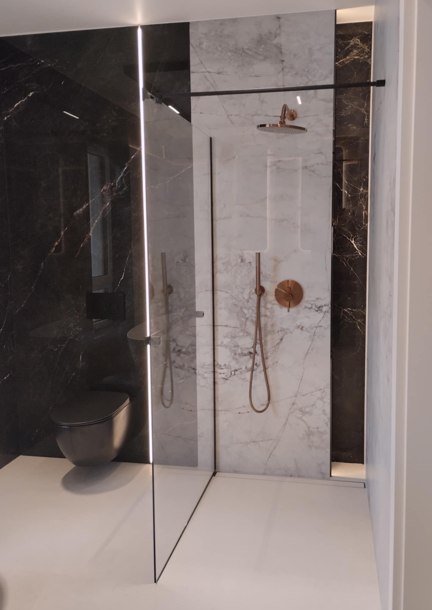 Nowoczesna łazienka z kabiną typu walk-in, wykończona marmurem w odcieniach bieli i czerni. Miedziana armatura i subtelne oświetlenie LED podkreślają elegancję wnętrza.