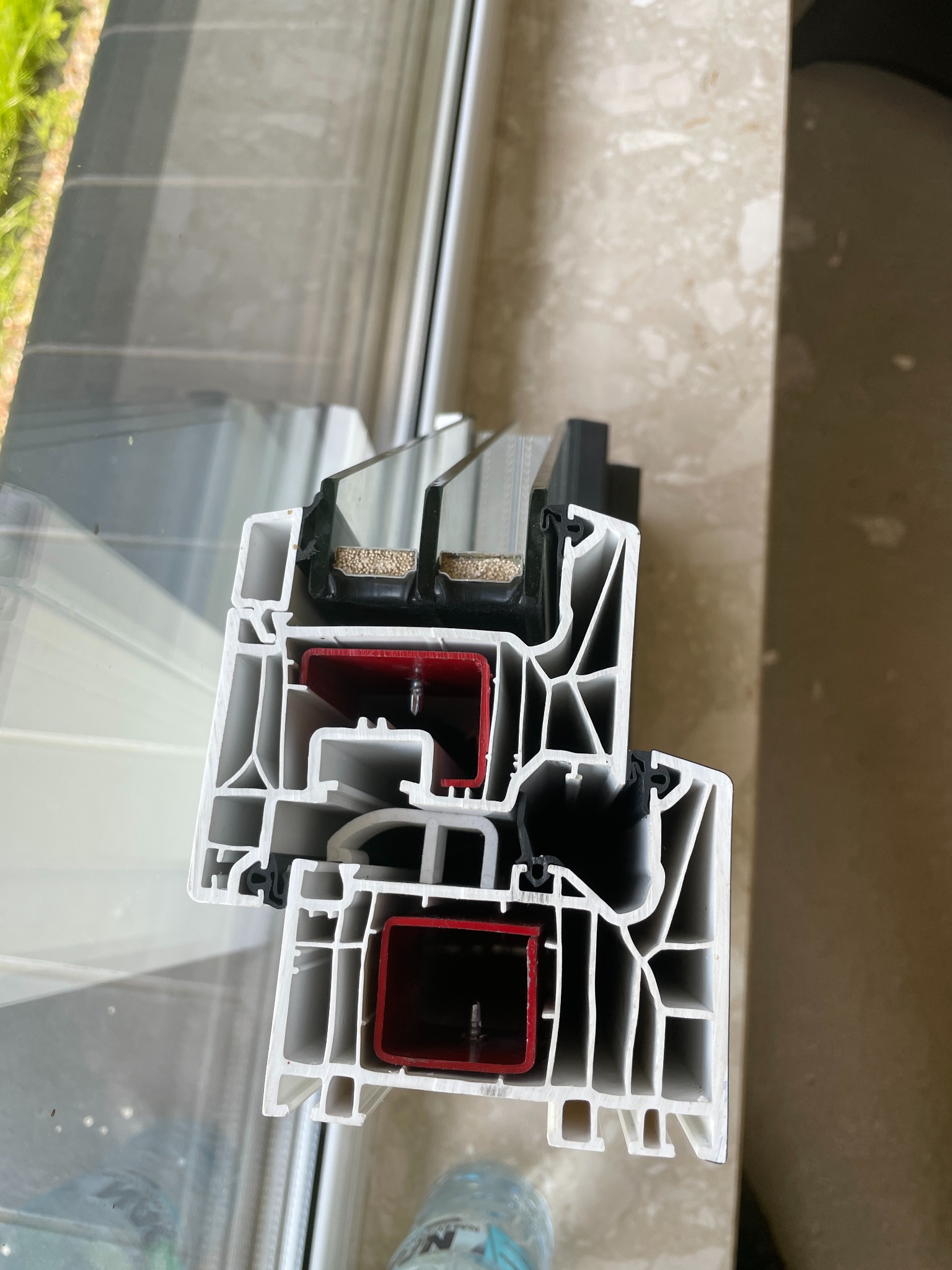 Przekrój okna PCV z widoczną strukturą wielokomorową, uszczelkami i szybami. Detal prezentuje izolację termiczną i budowę profilu okiennego.