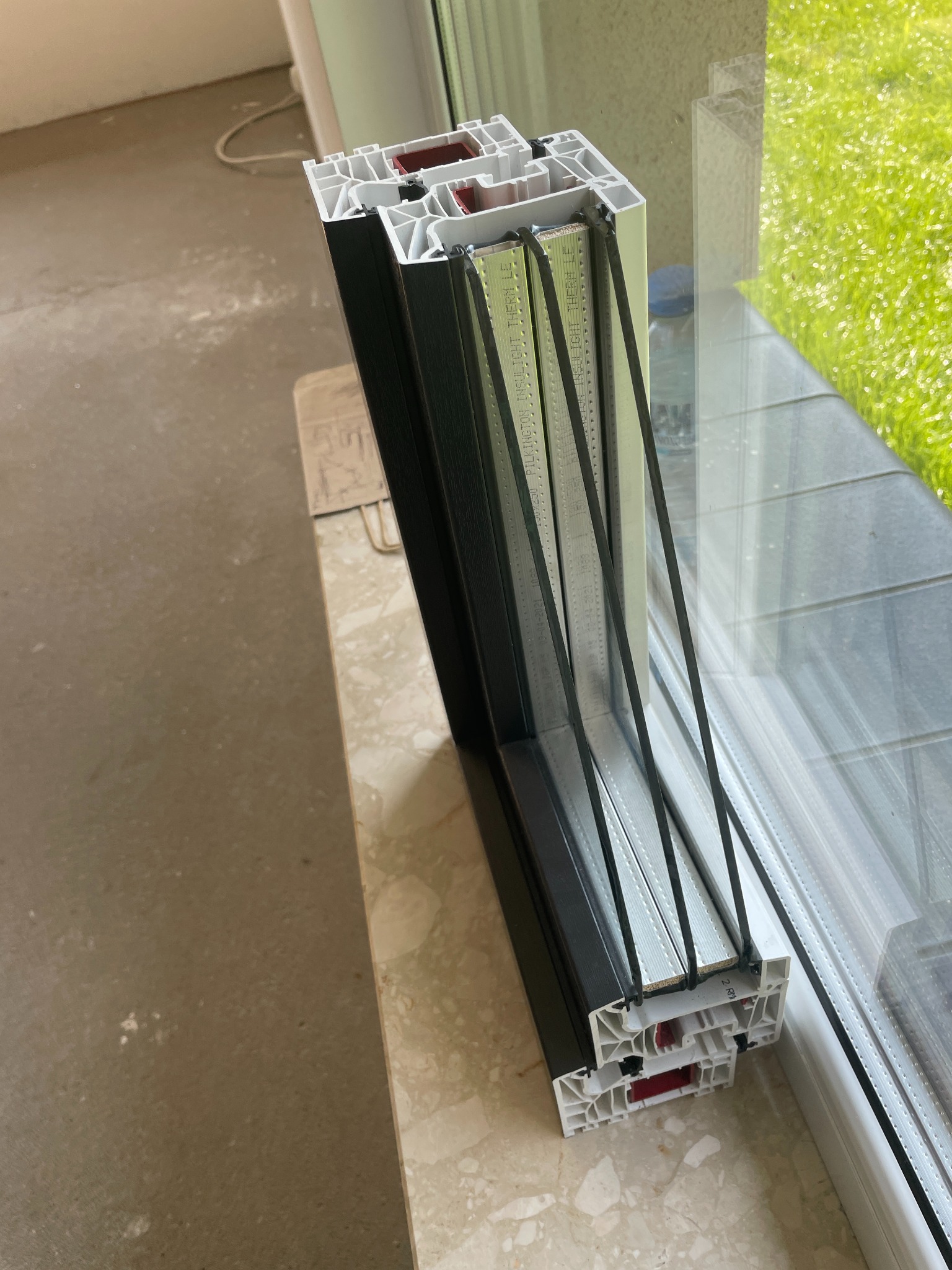 Przekrój okna z trzema szybami, ukazujący budowę profilu i izolację termiczną. Widoczne detale konstrukcyjne i materiały użyte w oknie.