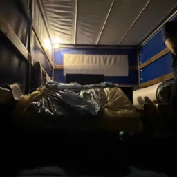 Wnętrze przestrzeni ładunkowej busa oświetlonej lampą, z workami i zabezpieczonymi meblami podczas transportu.