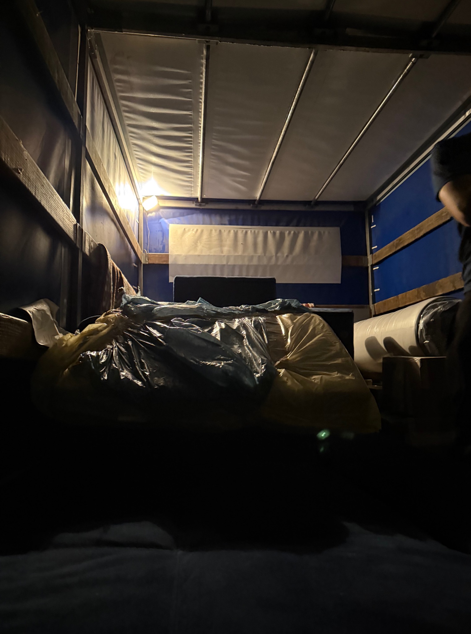 Wnętrze przestrzeni ładunkowej busa oświetlonej lampą, z workami i zabezpieczonymi meblami podczas transportu.