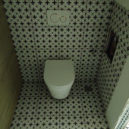 UJUT GROUP SPÓŁKA Z OGRANICZONĄ ODPOWIEDZIALNOŚCIĄ - Wnętrze łazienki po remoncie: biała toaleta w zabudowie, czarno-białe płytki na ścianach i podłodze z motywem krzyżyków. Widok z góry.