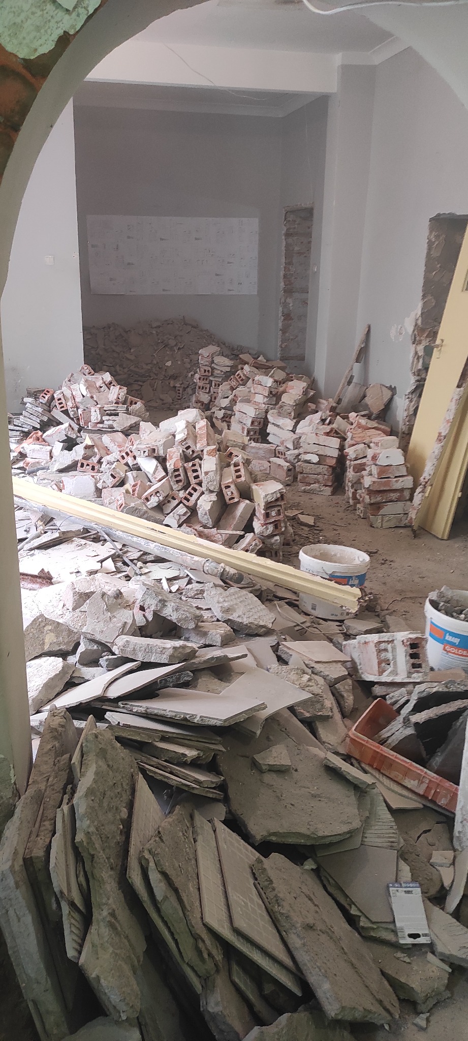 Wnętrze w trakcie demontażu: gruz, cegły i resztki materiałów budowlanych. Widoczne ślady po usuniętych elementach na ścianach i podłodze, przygotowanie do dalszych prac.