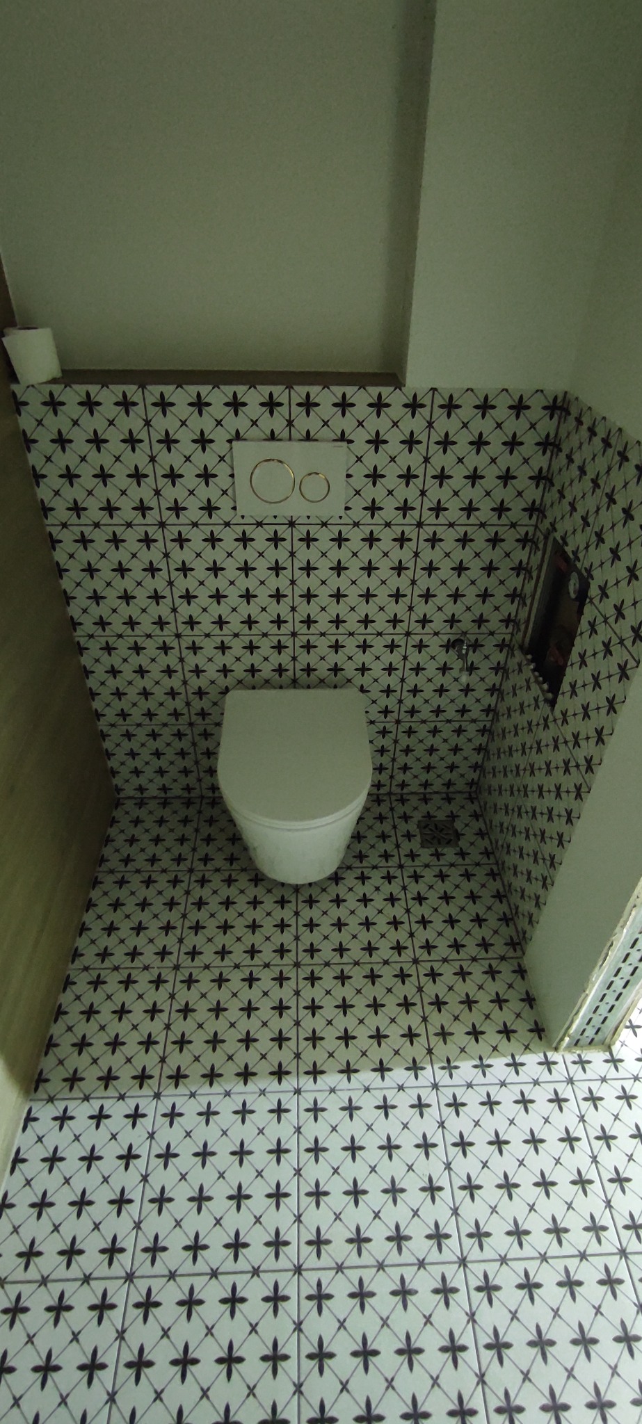 Wnętrze łazienki po remoncie: biała toaleta w zabudowie, czarno-białe płytki na ścianach i podłodze z motywem krzyżyków. Widok z góry.