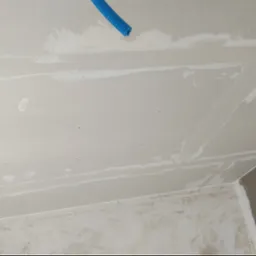 Sufit z płyt gipsowo-kartonowych w trakcie szpachlowania, widoczny niebieski przewód instalacyjny. Ściany częściowo przygotowane do malowania.