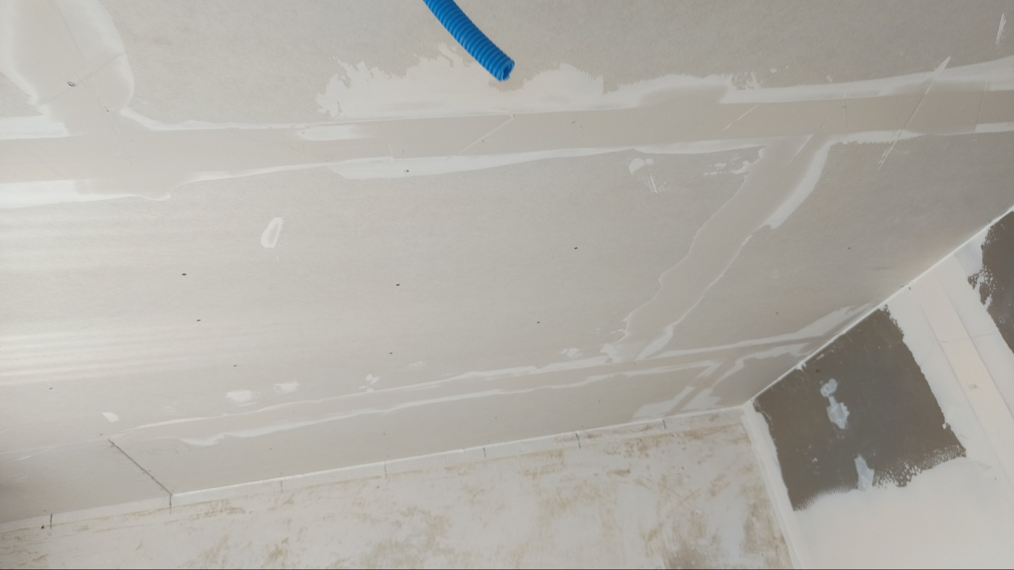 Sufit z płyt gipsowo-kartonowych w trakcie szpachlowania, widoczny niebieski przewód instalacyjny. Ściany częściowo przygotowane do malowania.