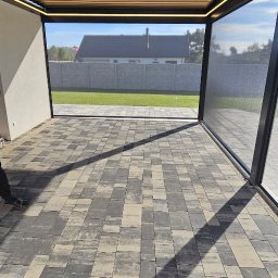 MIR TEAM MARIUSZ GRACZ, RAFAŁ TYMEK S.C. - Nowoczesna pergola metalowa z oświetleniem LED i roletami zewnętrznymi w Poznaniu. Widok z wnętrza na ogród i dom.