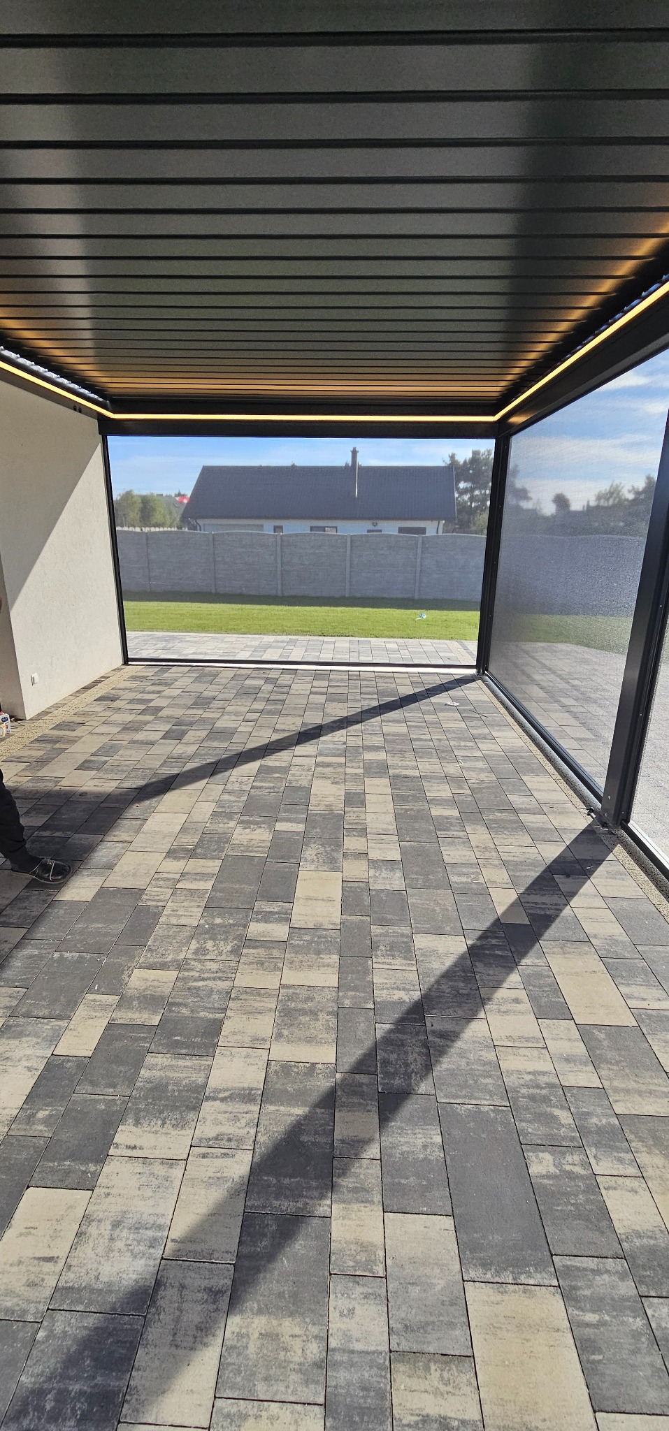 Nowoczesna pergola metalowa z oświetleniem LED i roletami zewnętrznymi w Poznaniu. Widok z wnętrza na ogród i dom.