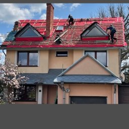 Janusz Makuch - Dom z częściowo zdjętym dachem, widoczna czerwona membrana i ekipa dekarzy w trakcie pracy. Na dachu okna dachowe.