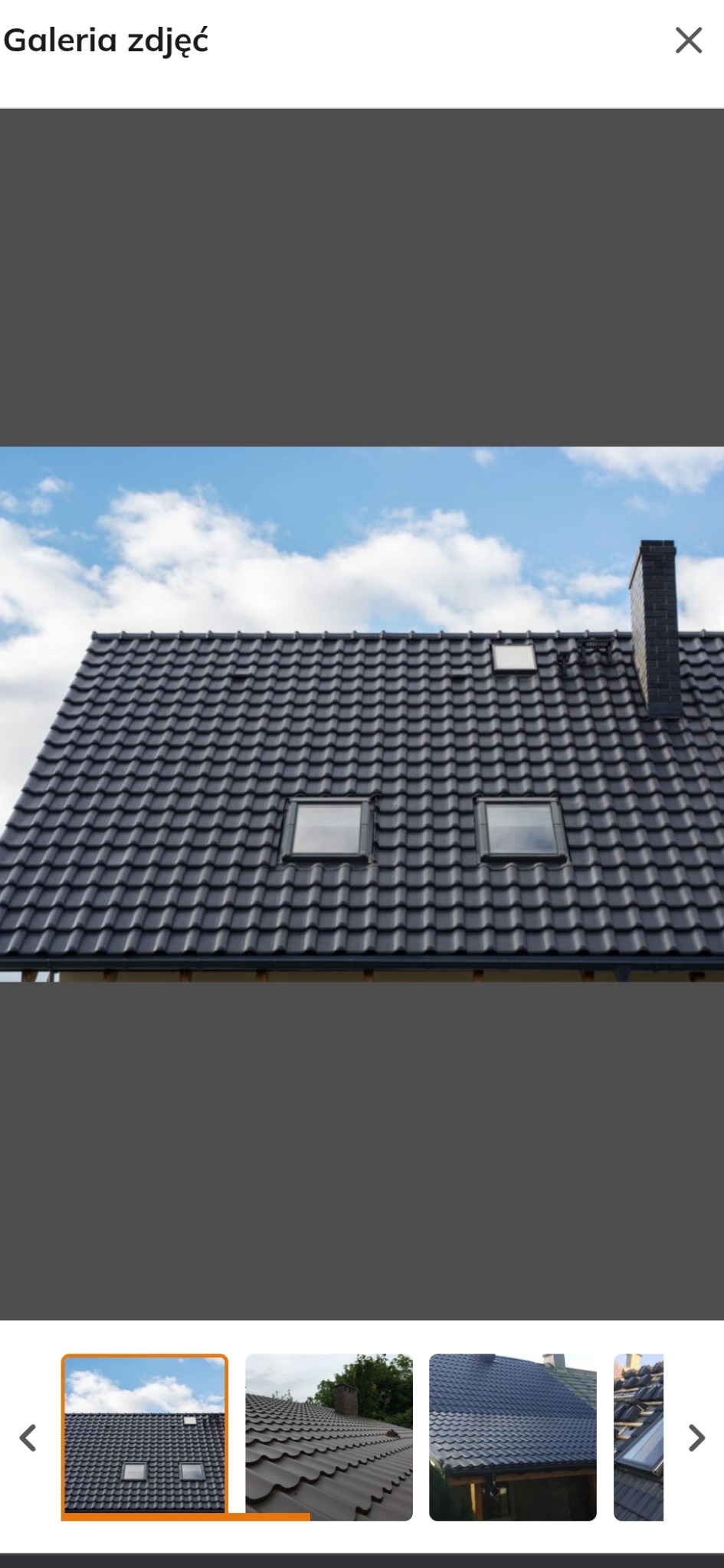 Ciemny dach z dachówką modułową, dwa okna dachowe i komin na tle błękitnego nieba z chmurami. Widok z dołu, podkreślający geometrię i jakość wykonania.