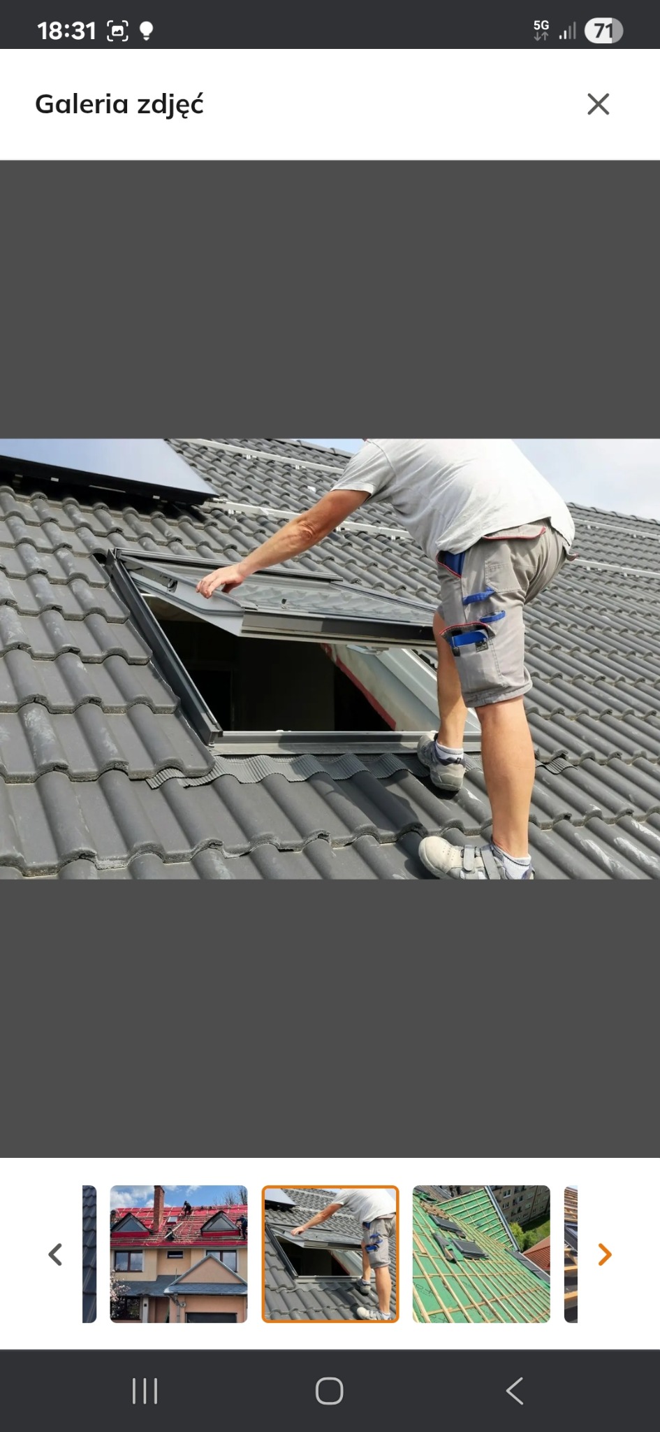 Dekarz montuje okno dachowe na dachu pokrytym szarą dachówką. Widoczny fragment nieba i fragment paneli słonecznych w tle. Praca dekarska w trakcie realizacji.