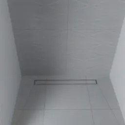 Minimalistyczna, biała kabina prysznicowa z odpływem liniowym, wykończona płytkami o wzorze rombów na ścianie.