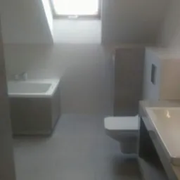 Wykończona łazienka na poddaszu w Pszowie z oknem dachowym, widoczne białe sanitariaty i szare płytki podłogowe.