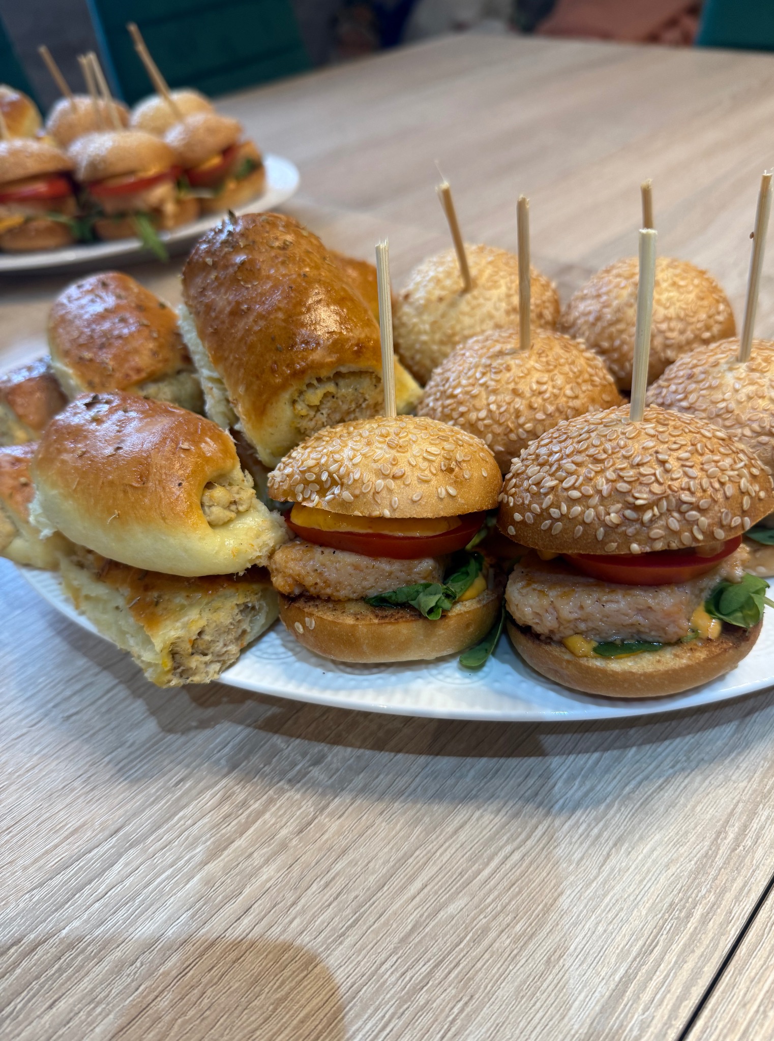 Wykwintny catering: mini burgery z sezamem i roladki z farszem na białym talerzu. Idealne na przyjęcia firmowe i święta.
