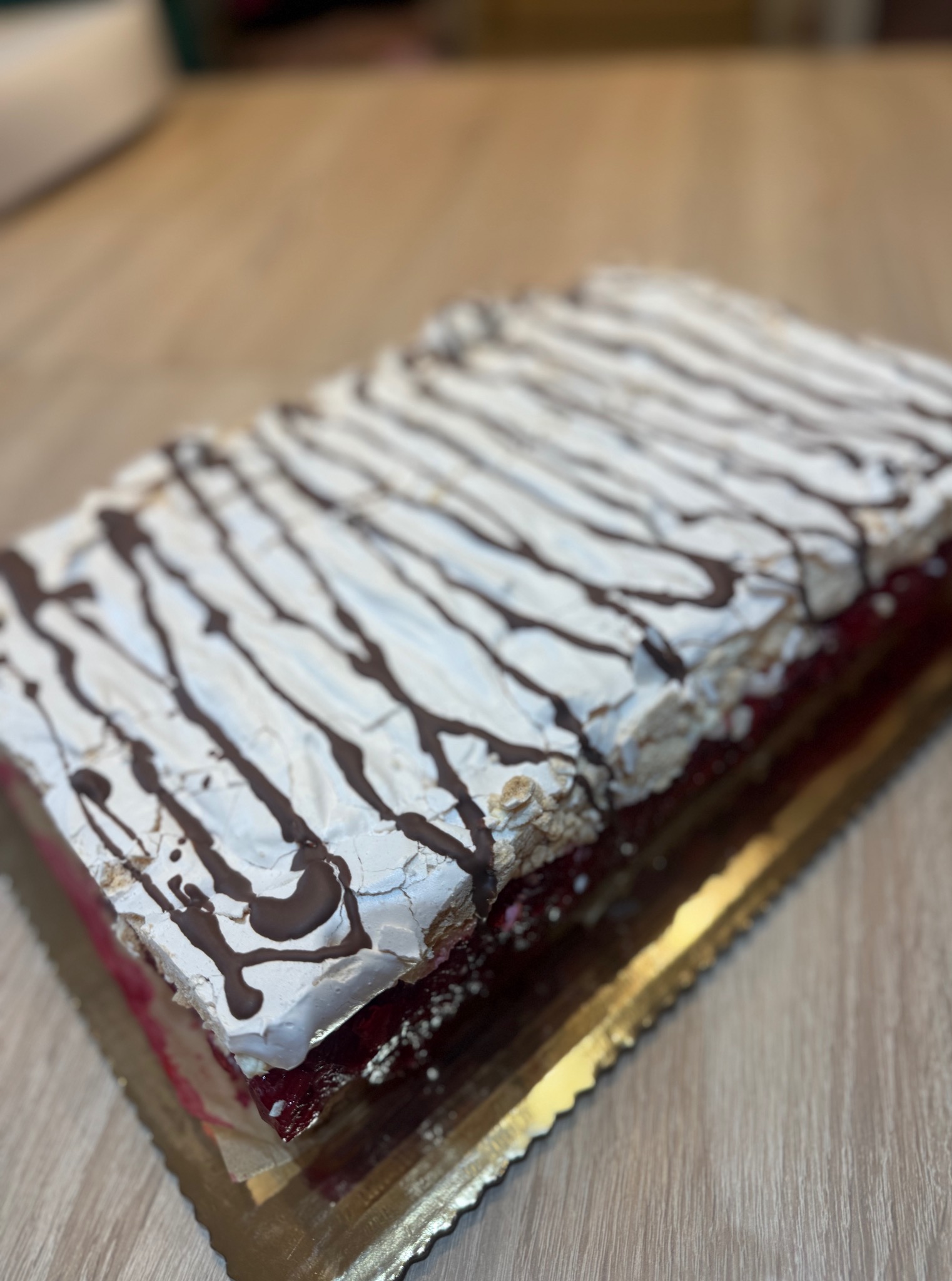 Kwadratowy tort bezowy z wiśniami na złotej tacy, dekorowany ciemną czekoladą. Widok z bliska, ukazujący warstwy i teksturę.