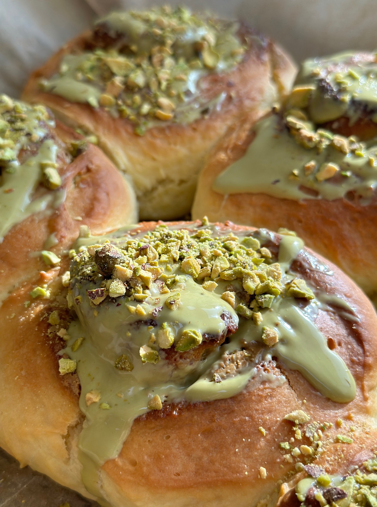 Puszyste bułeczki cynamonowe z pistacjowym lukrem i posypką z pistacji, prezentowane w zbliżeniu, ukazujące detale kremowego lukru i chrupiących orzechów.