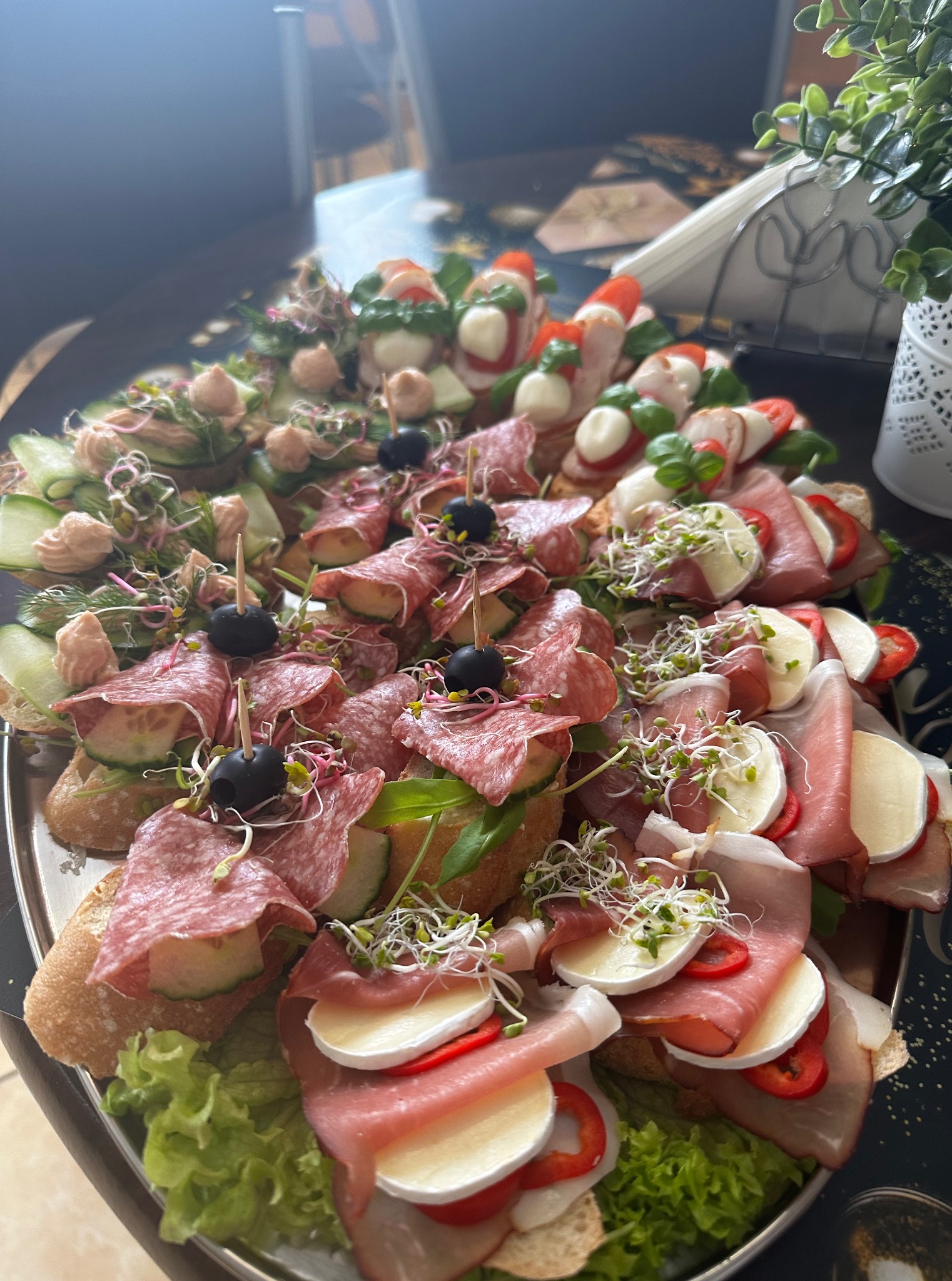 Elegancka taca z różnorodnymi kanapkami: salami, mozzarella z pomidorem i bazylią, ogórek z pastą, udekorowane kiełkami. Idealne na catering firmowy.