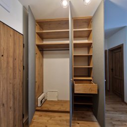 MODERNO Agnieszka Wieczorek - Otwarta szafa wnękowa z drewnianymi półkami i szufladą, szare drzwi, drewniana podłoga, widoczne oświetlenie sufitowe. Detal wnętrza.