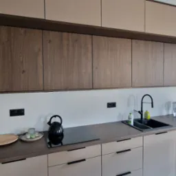 Nowoczesna kuchnia z drewnianymi i beżowymi frontami, czarnymi detalami i sprzętami. Widok na okno z budynkiem w tle. Minimalistyczny design.