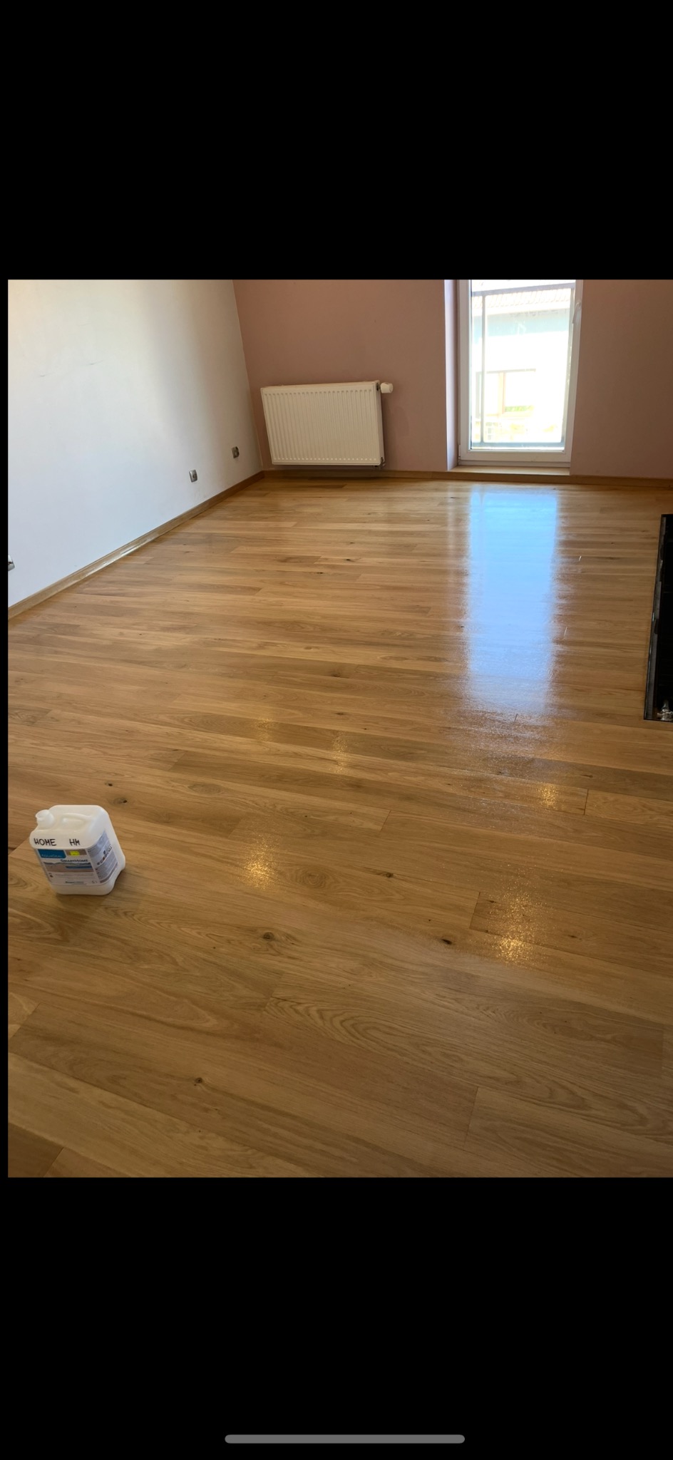 Parkiet po cyklinowaniu, widoczny pojemnik z preparatem do pielęgnacji drewna. Świeżo wycyklinowana podłoga z połyskiem, jasne ściany i okno.