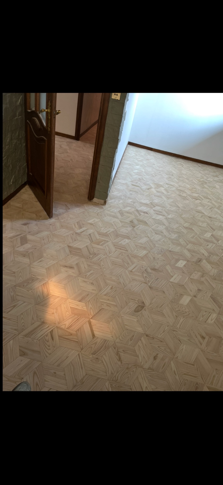 Parkiet w jodełkę francuską po renowacji, widoczny fragment otwartych drzwi i ściana z cegieł. Na podłodze cień rzucany przez słońce.