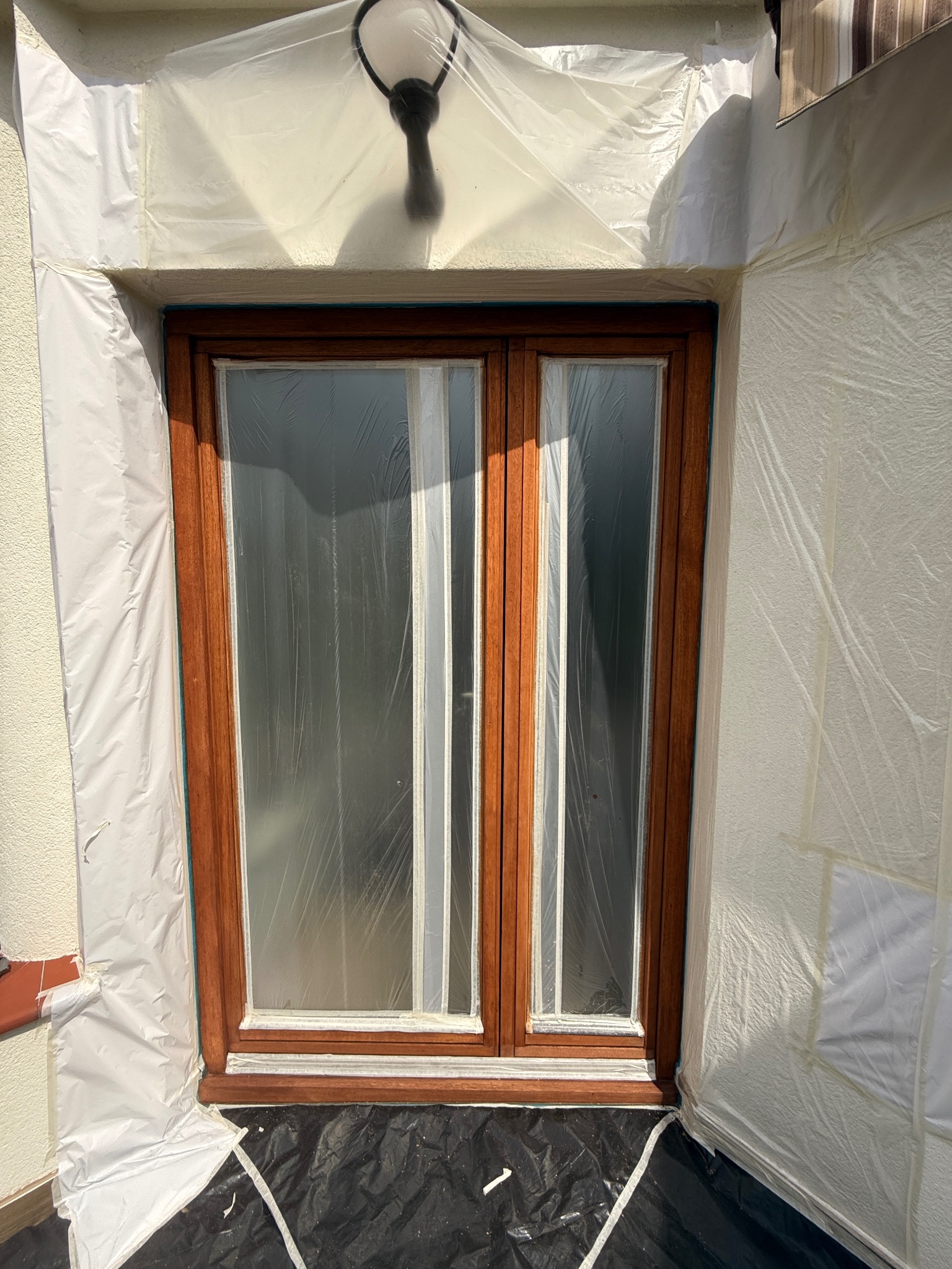 Drewniane okno zabezpieczone folią malarską przed renowacją. Widoczne detale ramy i szyb. Ochrona podczas prac malarskich.