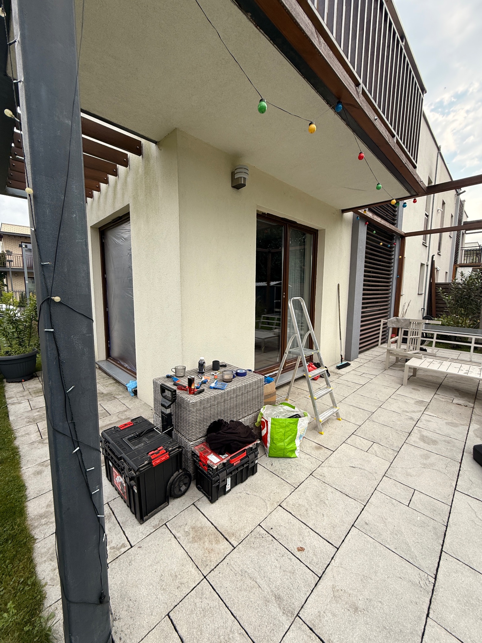 Przygotowania do montażu okien balkonowych w Łodzi. Widoczne narzędzia, drabina i okno zabezpieczone folią. Praca na zewnątrz budynku.