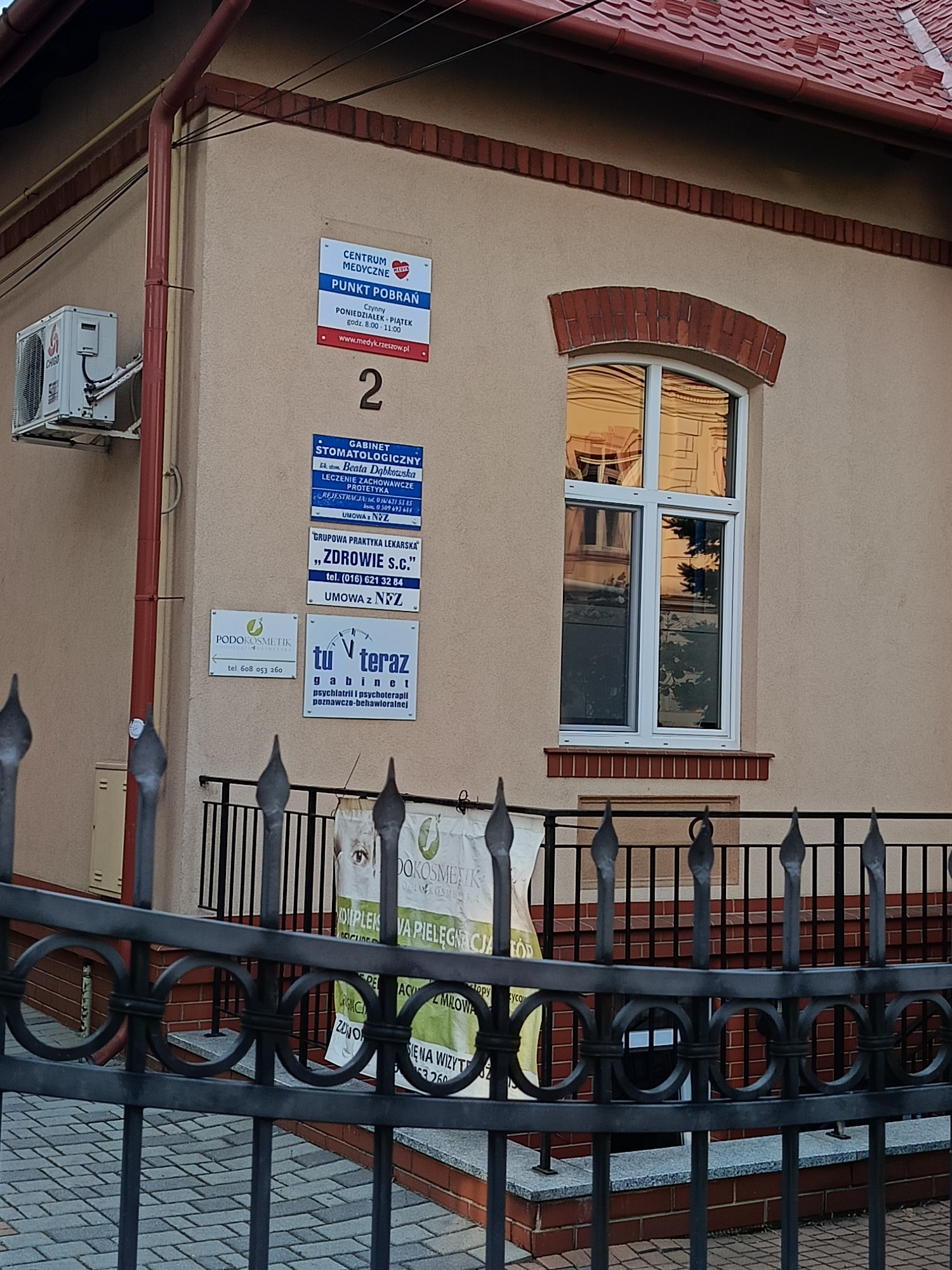 Budynek medyczny z szyldami: punkt pobrań, gabinet stomatologiczny, praktyka lekarska, gabinet psychoterapii poznawczo-behawioralnej, podokosmetologiczny.
