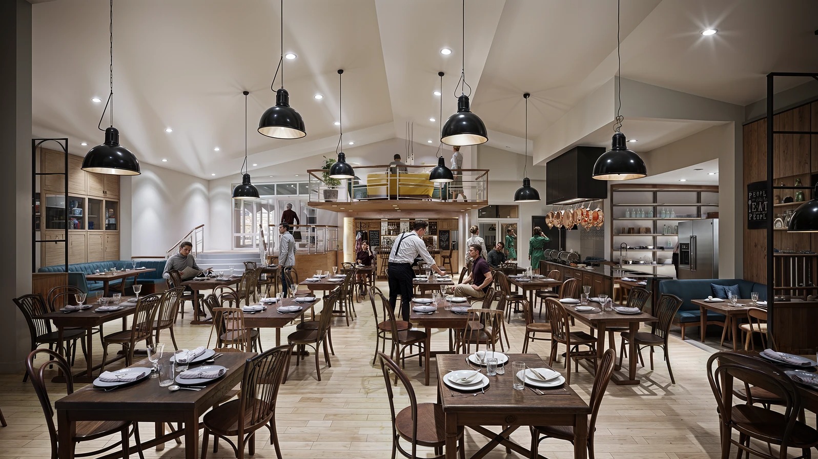 Wnętrze restauracji z drewnianymi stołami i krzesłami, oświetlone wiszącymi lampami. Na antresoli bar i goście. Aranżacja przestrzeni z dbałością o detale.